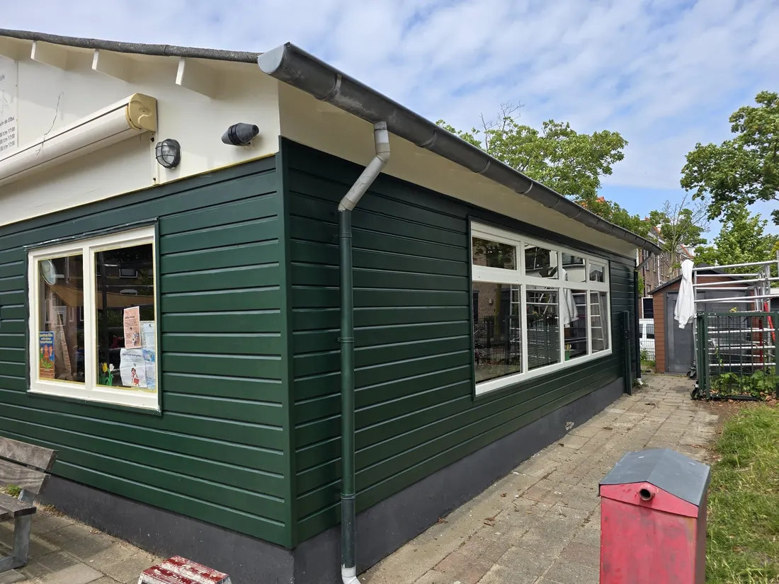 Donkergroene gevelbekleding met witte dakrand en raamkozijnen