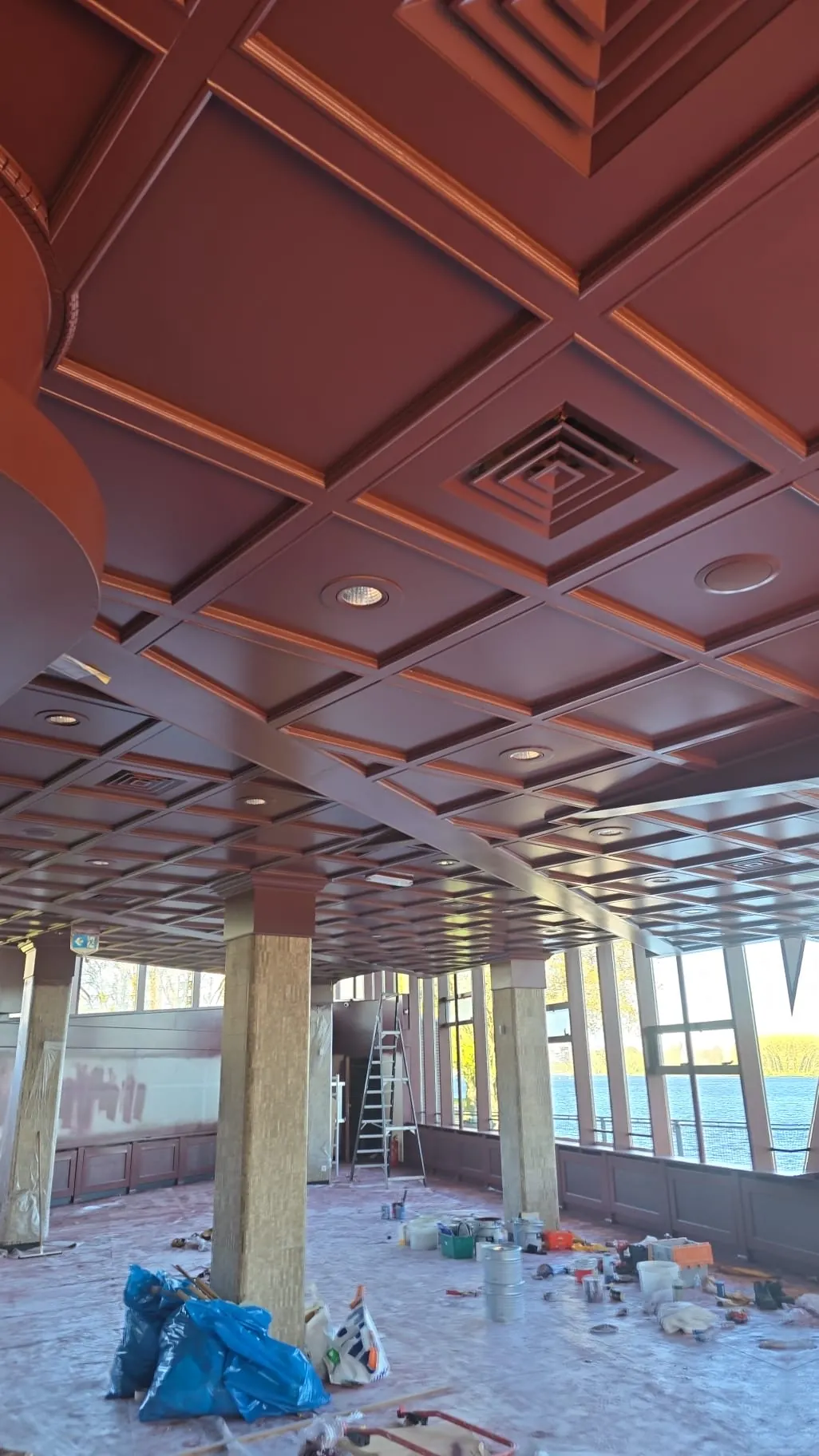 Roodbruin paneelplafond met sierlijsten boven een afgedekte werkruimte