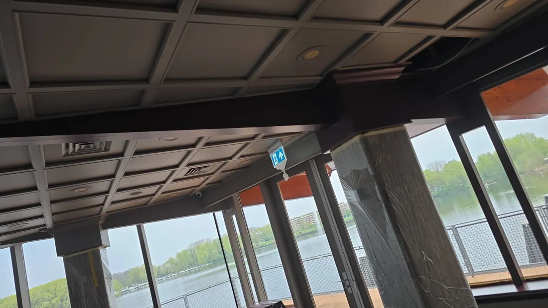 Grijs paneelplafond met donkere balken bij grote ramen